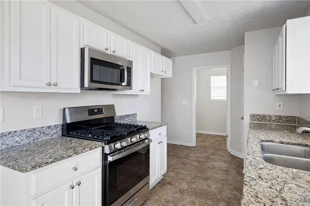 a kitchen with stainless steel appliances granite countertop white cabinets a stove a microwave and a sink
