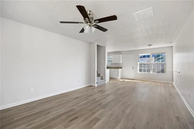 an empty room with wooden floor ceiling fan and windows