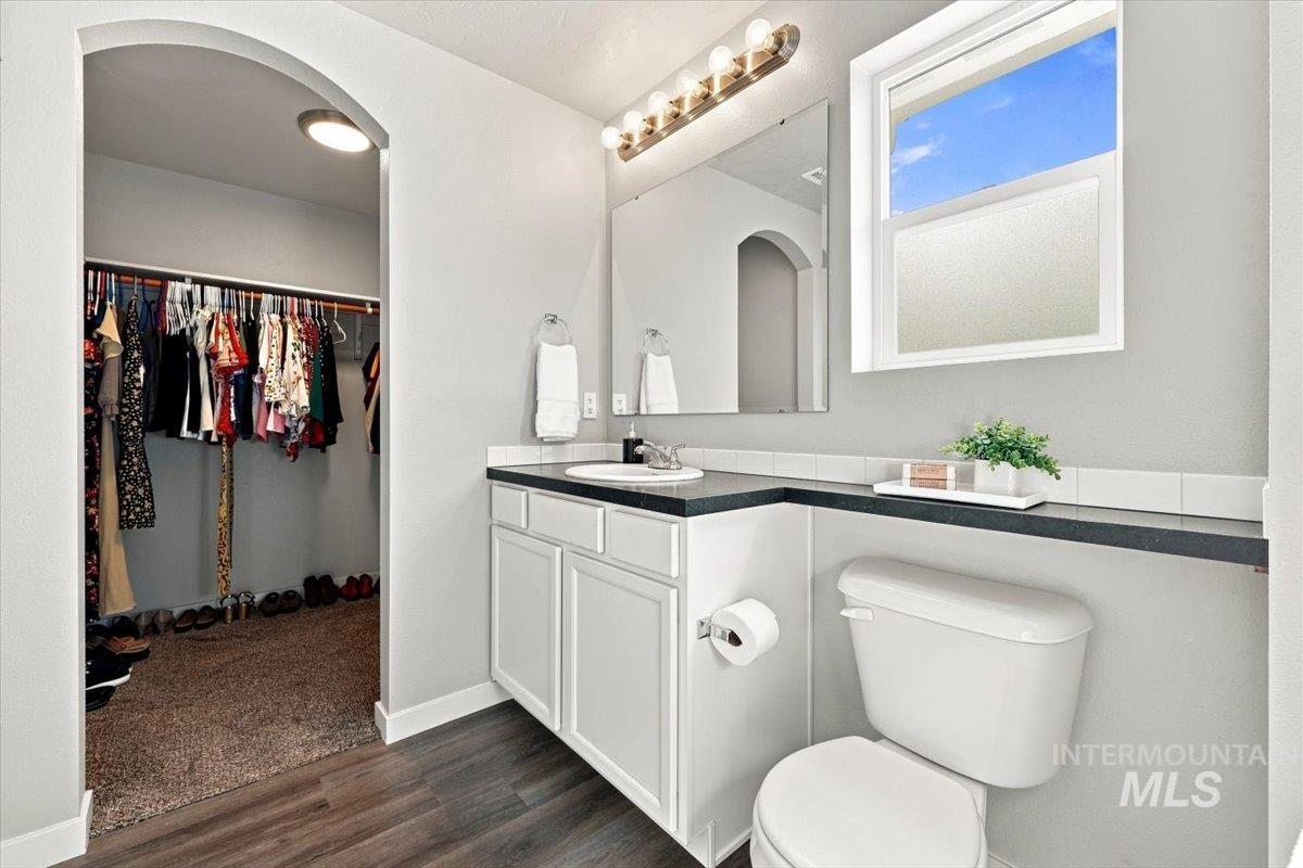 696 East Springloyd Street Meridian, ID 83642 - Photo 27 of 37 Vanity with white cabinetry and dark countertop, window with privacy glass, arched doorway, wood-finish flooring, and a walk-in closet with carpeted flooring