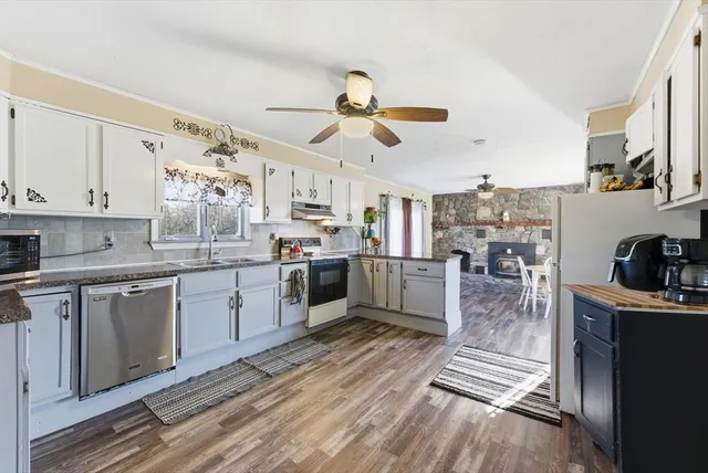 a kitchen with granite countertop a refrigerator a sink dishwasher a stove and white cabinets with wooden floor