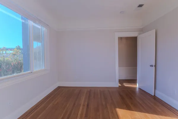 a view of an empty room with wooden floor and a window