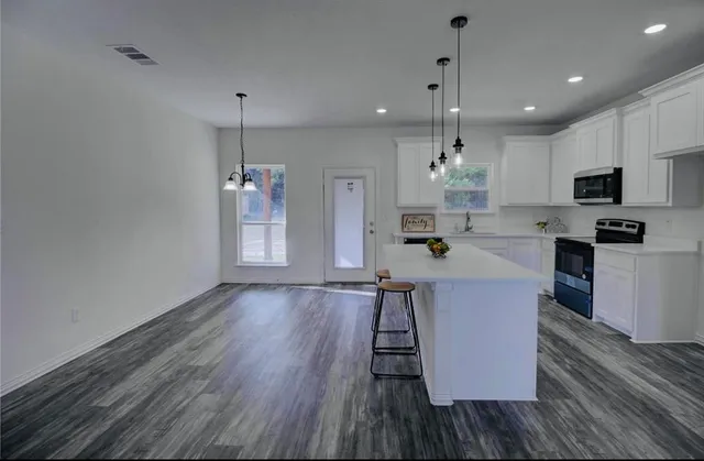a kitchen with stainless steel appliances granite countertop a refrigerator a stove top oven a sink dishwasher and a dining table with wooden floor