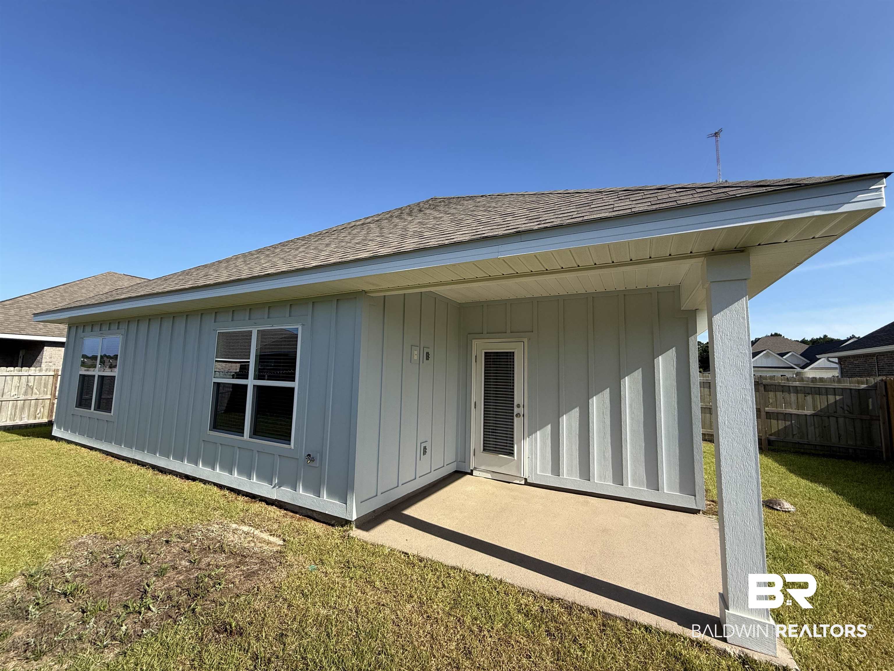 23247 Lieutenant Avenue Foley, AL 36535 - Photo 39 of 47 Rear exterior featuring light-colored board and batten siding, multiple windows, a covered patio with concrete flooring, and a glass-paned door
