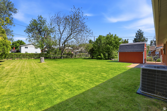 2348 North 770 West Clinton, UT 84015 - Photo 20 of 25 Expansive green lawn featuring a red storage shed with a shingled roof, mature trees, a privacy hedge, and an air conditioning unit