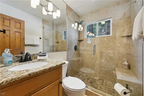 a bathroom with a granite countertop sink a toilet a mirror and shower