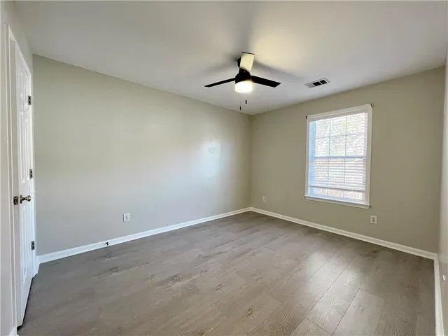 an empty room with wooden floor fan and windows
