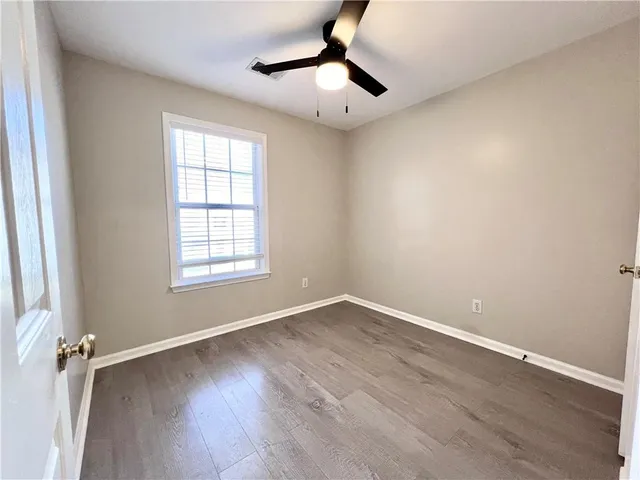 an empty room with wooden floor chandelier fan and windows