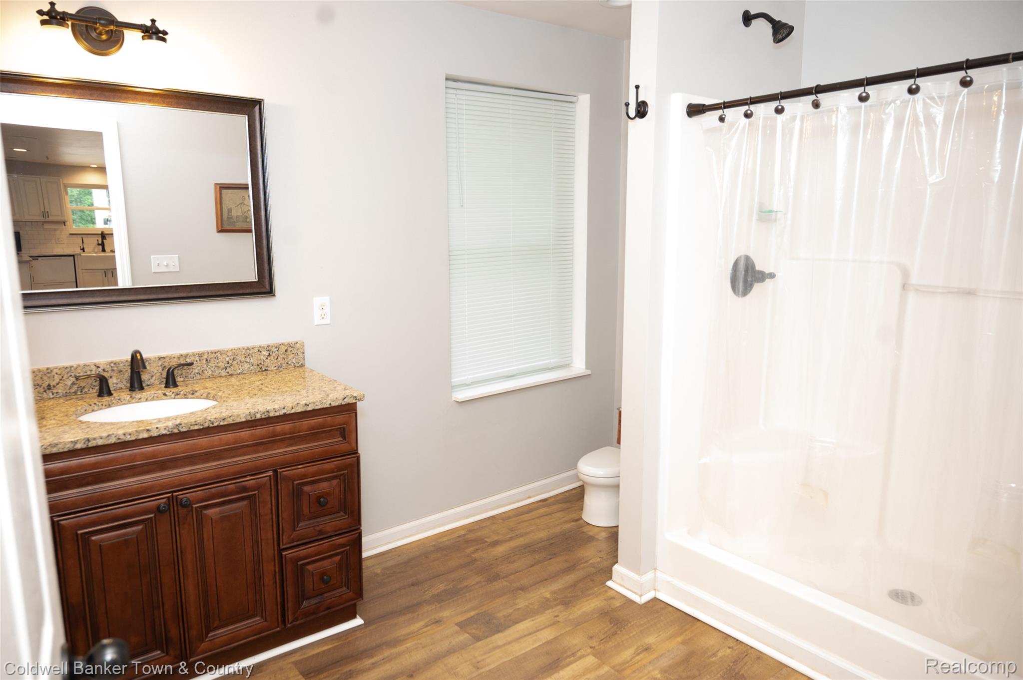 6150 North Fleming Road Howell, MI 48855 - Photo 15 of 23 Bathroom featuring a dark wood-finish vanity with a speckled countertop, a rectangular mirror, and wood-finish flooring