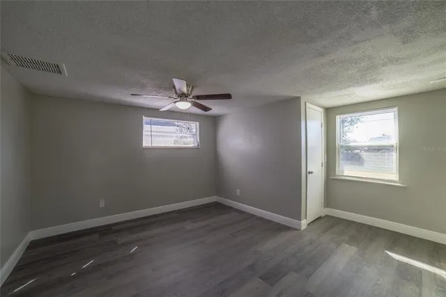 an empty room with wooden floor fan and windows