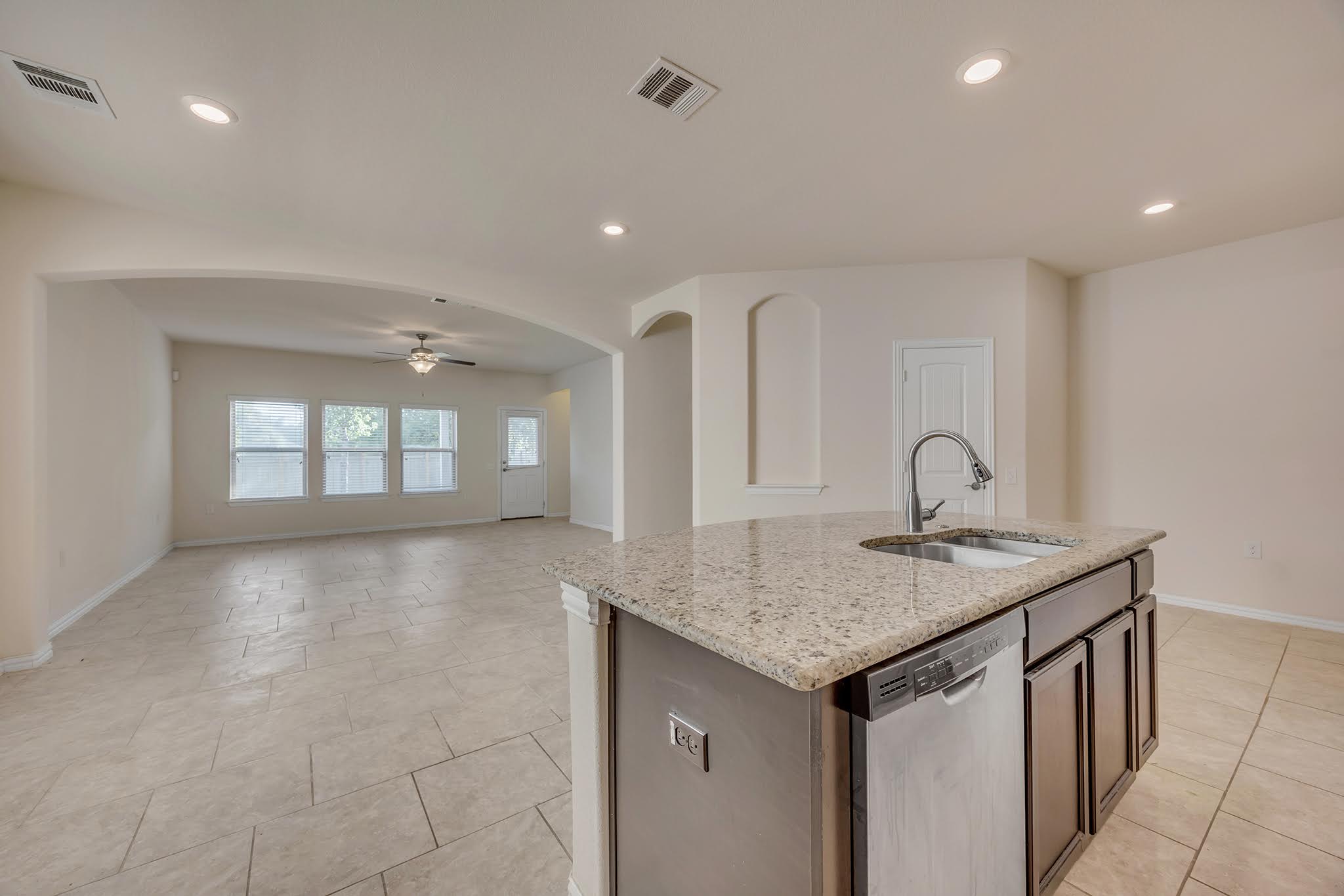 7212 Vail Ridge Street Austin, TX 78744 - Photo 6 of 26 A well-lit interior features a central kitchen island with a sink, overlooking a spacious living area with tiled flooring.