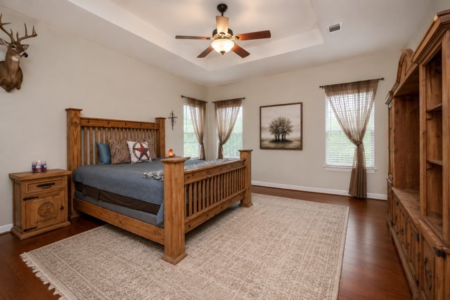 27644 Spring Hill Road Hempstead, TX 77445 - Photo 25 of 43 What a marvelous place for peace and repose! This primary suite invites super-sized pieces with amazing floor and wall space and bright, natural light. Note the tray ceiling theme, here too. This view has been AI enhanced to remove some of the furniture and add rug.