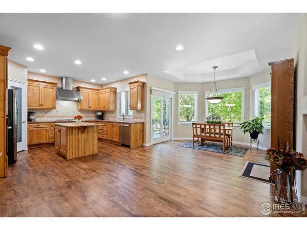 a kitchen with stainless steel appliances kitchen island granite countertop a refrigerator a stove a sink a dining table and chairs with wooden floor