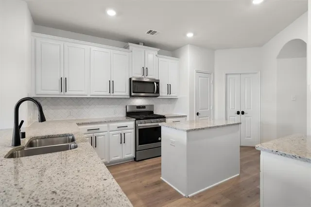a kitchen with stainless steel appliances granite countertop a stove top oven a sink and white cabinets