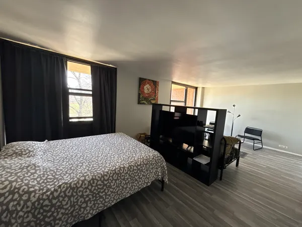 a bedroom with a bed and dresser with wooden floor