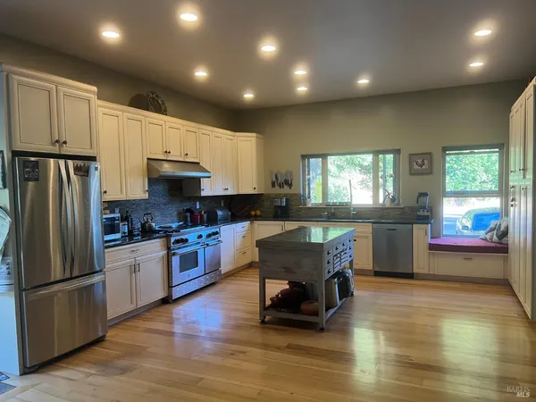 a kitchen with stainless steel appliances granite countertop a refrigerator a stove top oven a sink dishwasher and white cabinets with wooden floor