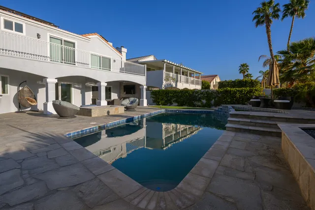 a view of a white house with a big yard potted plants and a table