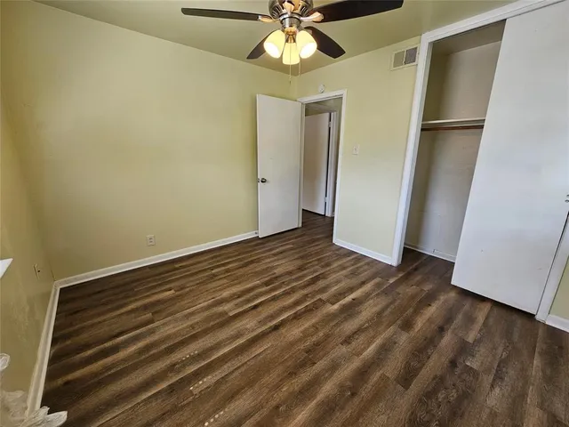 a view of an empty room with wooden floor and a ceiling fan
