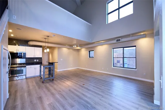 an empty room with wooden floor and a kitchen