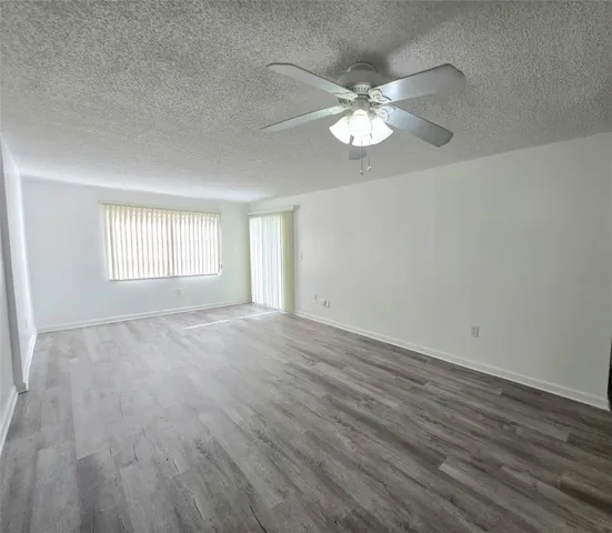 an empty room with wooden floor fan and windows