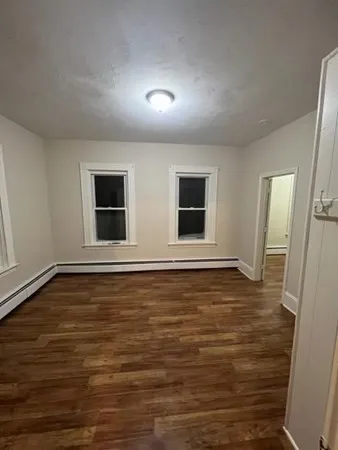 a view of an empty room with wooden floor and windows