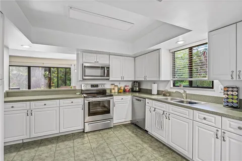 a kitchen with white cabinets appliances a sink and a window