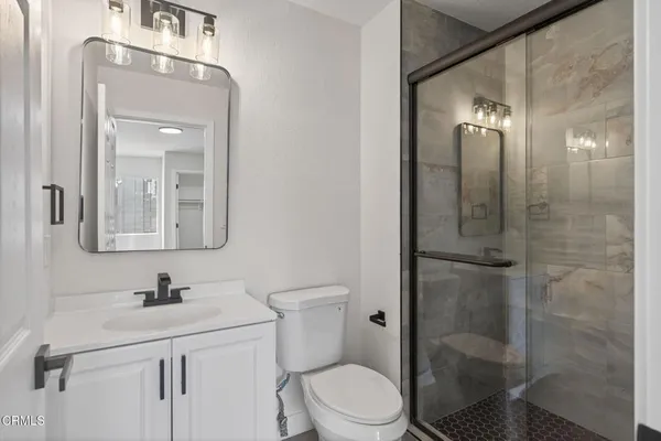 a bathroom with a toilet a sink a glass door a shower and a mirror