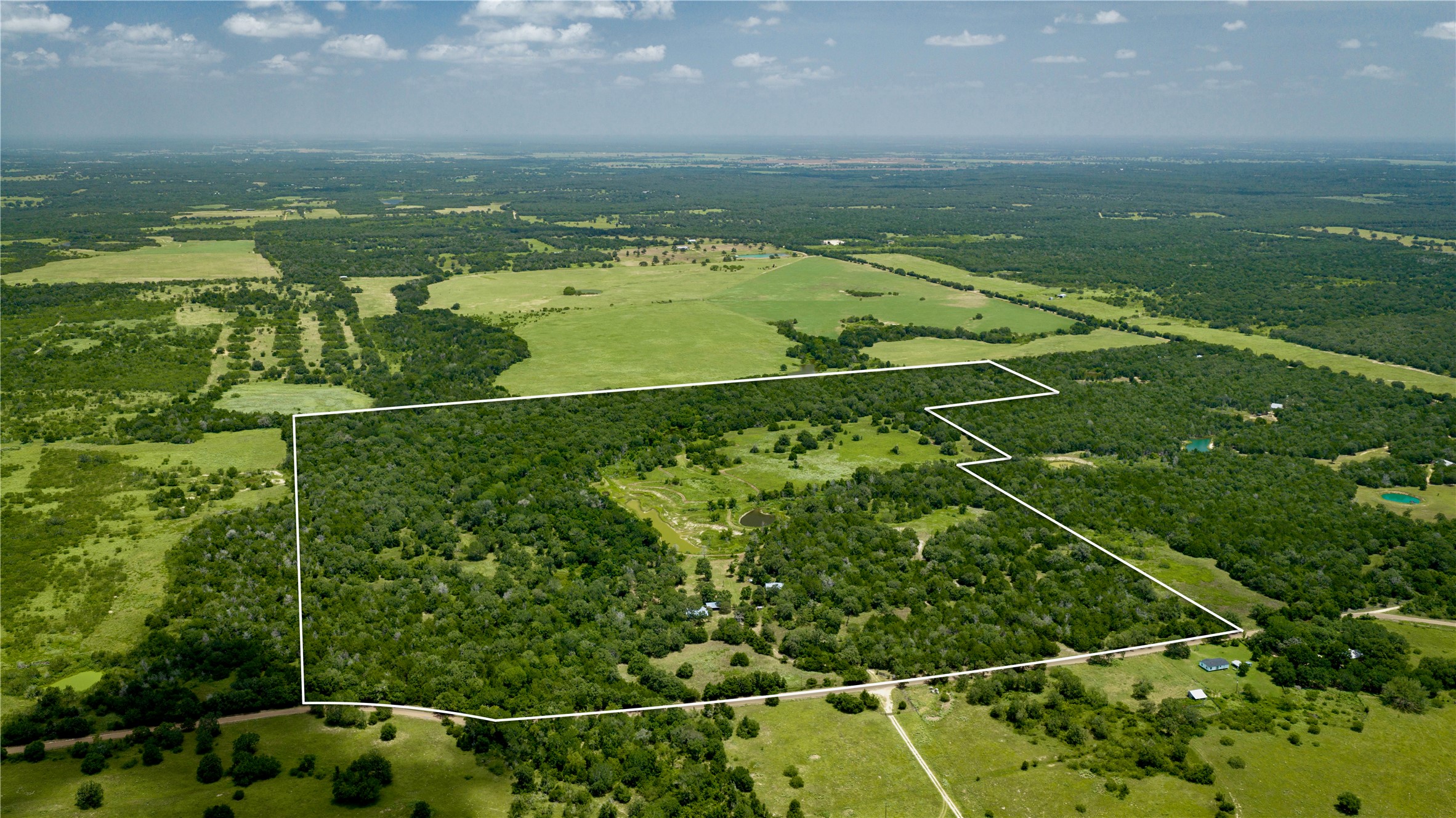 7221 West Old Lockhart Road Muldoon, TX 78949 - Photo 38 of 38 A vast expanse of wooded acreage and cleared pastures unfolds under a bright summer sky.