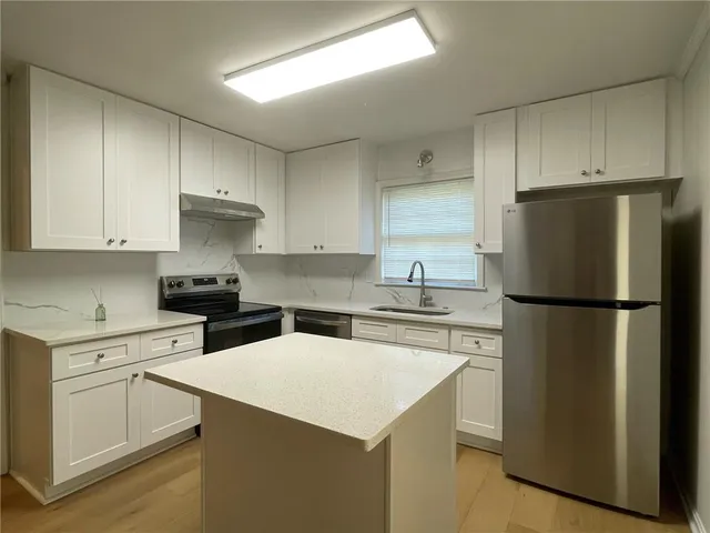 a kitchen with stainless steel appliances a refrigerator a stove a sink and white cabinets