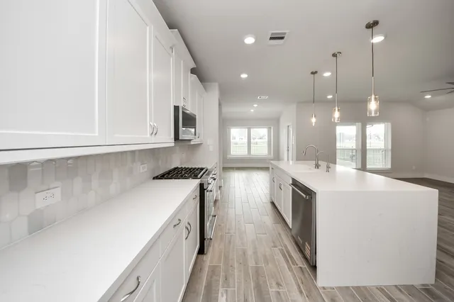 a large white kitchen with a white stove top oven a sink dishwasher and a refrigerator with wooden floor