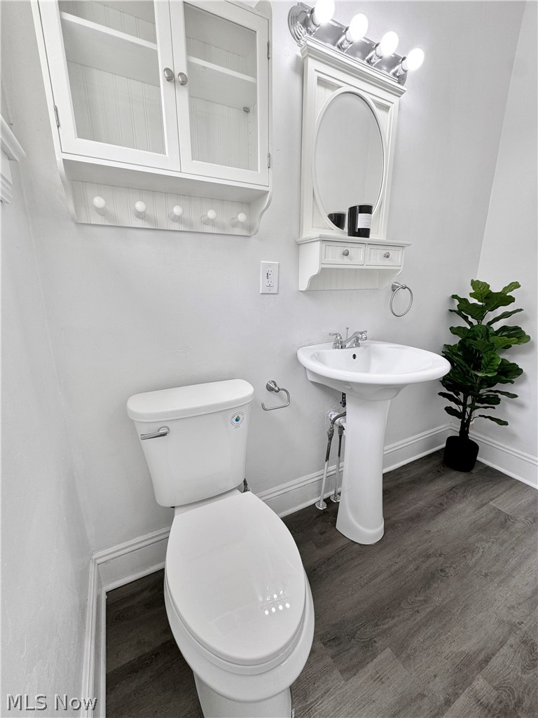 977 Nathaniel Road Cleveland, OH 44110 - Photo 15 of 22 Pedestal sink with chrome fixtures, wood-finish flooring, white wall-mounted storage cabinet, and a framed oval mirror with integrated lighting