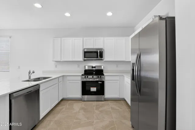a kitchen with stainless steel appliances granite countertop a refrigerator a sink a stove top oven and white cabinets