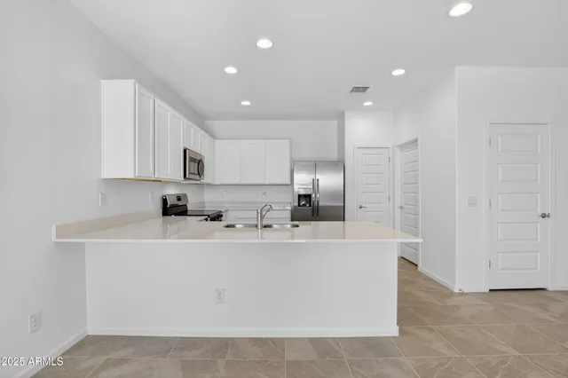 a large white kitchen with stainless steel appliances a sink a microwave a refrigerator and cabinets