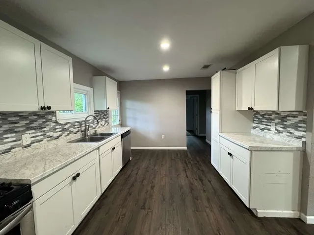 a large white kitchen with granite countertop a sink and dishwasher a stove with wooden floor