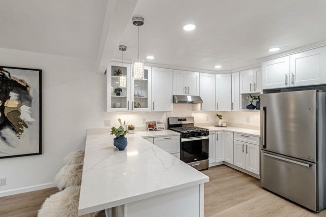 a kitchen with refrigerator a stove a sink and white cabinets with wooden floor