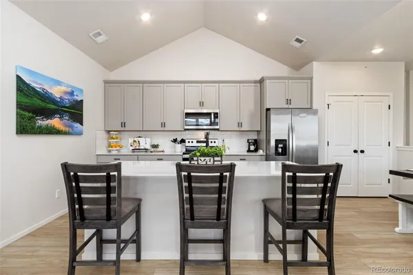 a kitchen with stainless steel appliances a refrigerator stove a sink a dining table and chairs with wooden floor