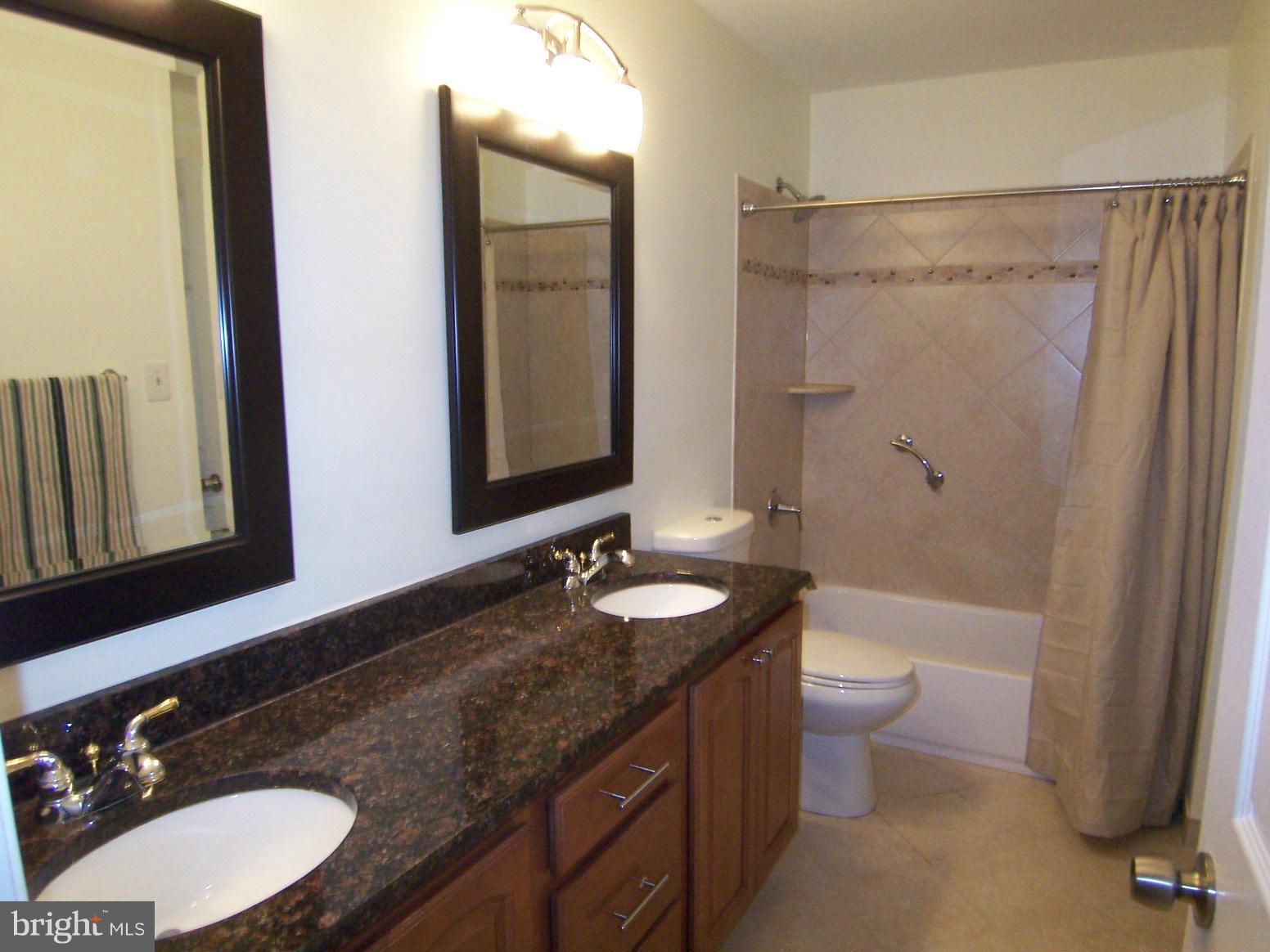 9104 Rookings Court Springfield, VA 22153 - Photo 15 of 22 a bathroom with a granite countertop sink toilet a large mirror a bathtub and shower