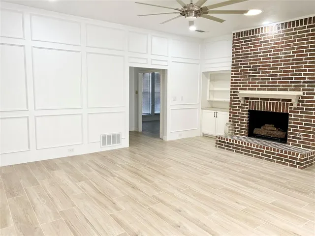 an empty room with wooden floor a ceiling fan a fireplace and windows