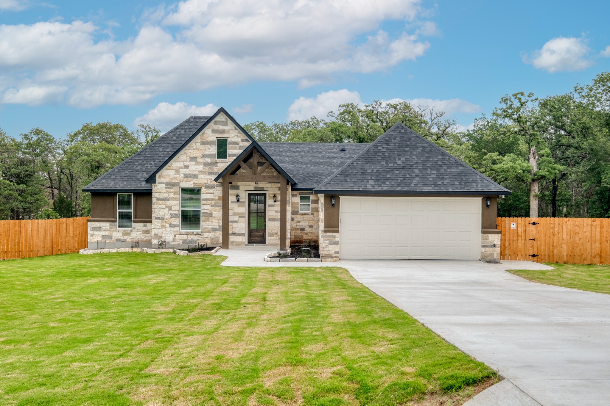 116 Pine Point Cove Elgin, TX 78621 - Photo 1 of 27 Stone and stucco exterior featuring a prominent gabled entry with timber accents, a two-car garage, and a manicured lawn