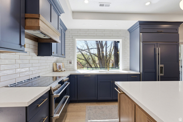 7935 Mustang Loop Road Park City, UT 84098 - Photo 20 of 60 Kitchen featuring dark blue cabinetry with gold-tone hardware, white countertops, a built-in refrigerator, and a stainless steel range with a custom wood-finished range hood