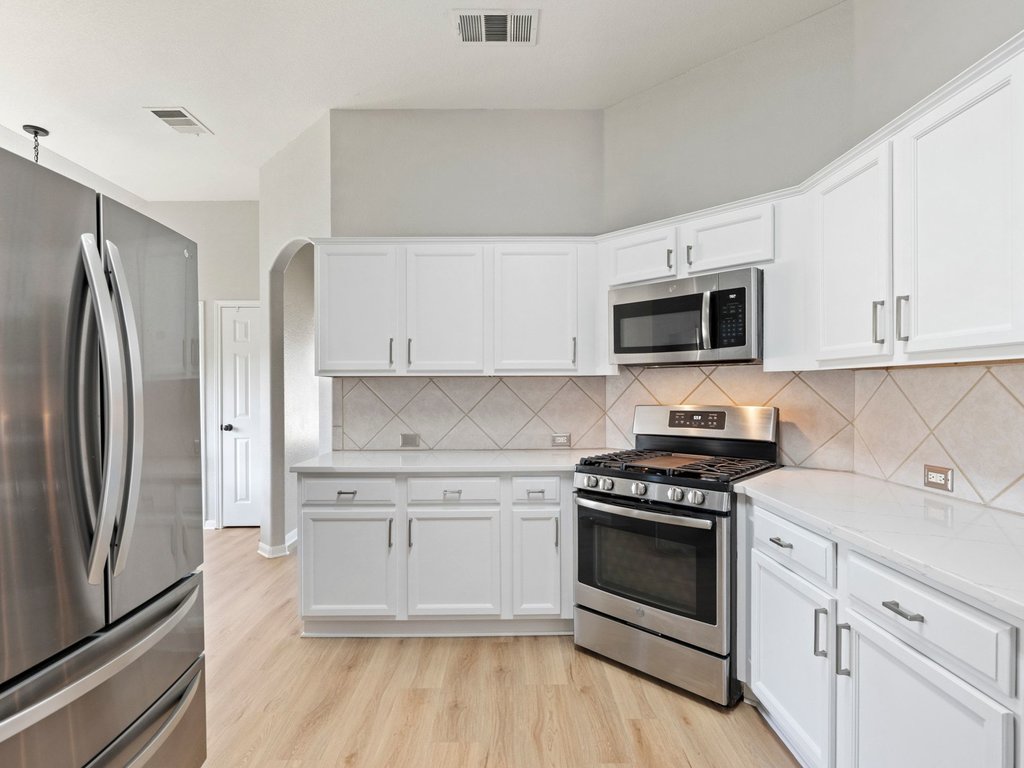 1201 Ridgewood Drive Leander, TX 78641 - Photo 7 of 28 Kitchen featuring stainless steel appliances, white cabinetry, light wood-style flooring, and arched walkways