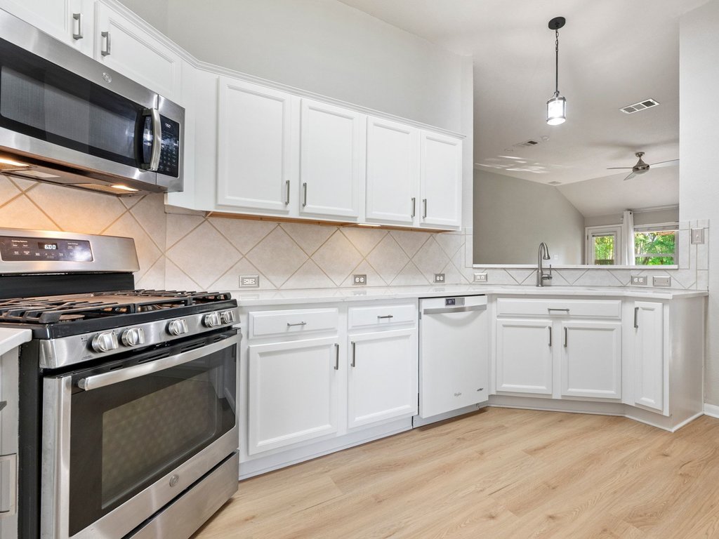 1201 Ridgewood Drive Leander, TX 78641 - Photo 9 of 28 Kitchen featuring stainless steel appliances, decorative backsplash, white cabinets, light wood-style floors, and vaulted ceiling
