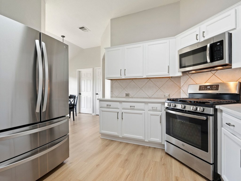1201 Ridgewood Drive Leander, TX 78641 - Photo 10 of 28 Kitchen featuring stainless steel appliances, light wood-type flooring, white cabinets, tasteful backsplash, and vaulted ceiling