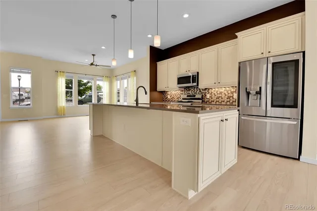 a kitchen with stainless steel appliances kitchen island granite countertop a stove top oven a sink a refrigerator white cabinets and wooden floor