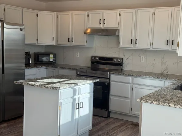 a kitchen with stainless steel appliances granite countertop a stove a refrigerator and a white cabinets