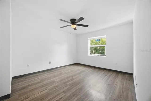 an empty room with wooden floor ceiling fan and windows