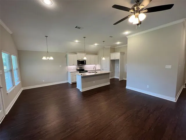 an empty room with wooden floor a ceiling fan and kitchen view