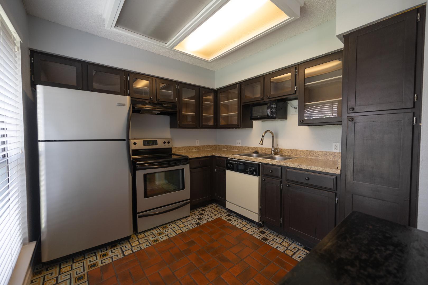 2110 Rio Grande Street, Unit 307 Austin, TX 78705 - Photo 5 of 12 A corner kitchen showcases sleek stainless appliances and warm terracotta flooring, ready for culinary endeavors.