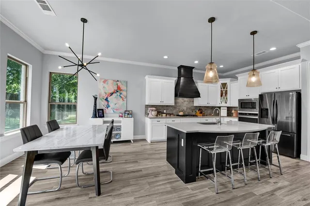 a kitchen with stainless steel appliances kitchen island granite countertop a stove a refrigerator a sink a dining table and chairs with wooden floor