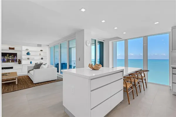 a large white kitchen with stainless steel appliances granite countertop a stove a sink a refrigerator and a dining table with wooden floor