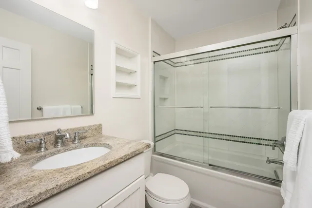 a bathroom with a granite countertop bathtub shower sink vanity and toilet